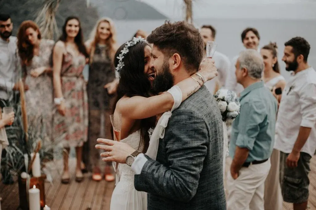 Happy newlyweds embrace during their outdoor wedding celebration surrounded by friends and family.