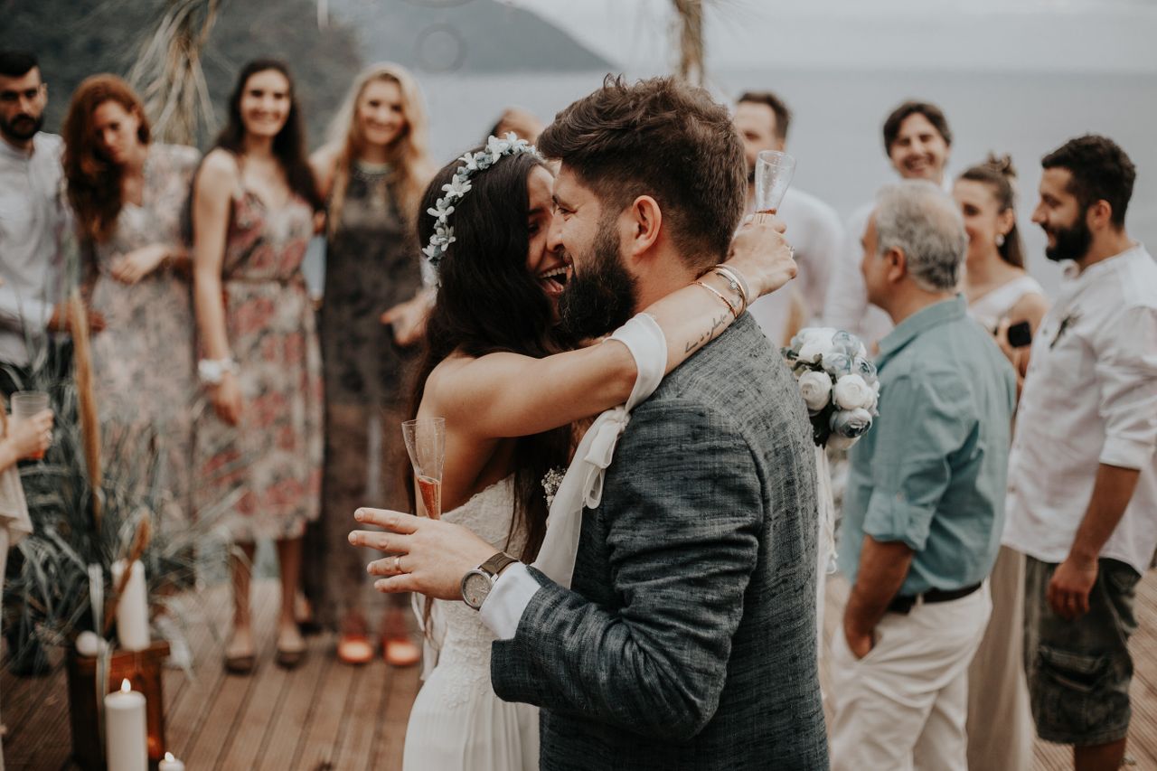 Happy newlyweds embrace during their outdoor wedding celebration surrounded by friends and family.