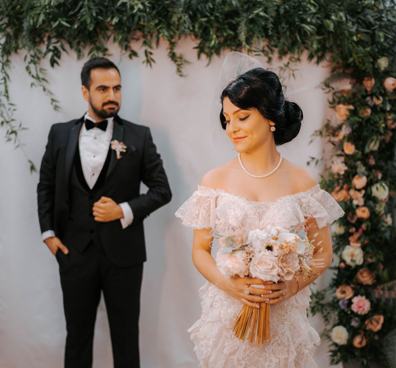 Bride and groom posing under a beautiful floral arch during a wedding ceremony, exuding elegance and grace.