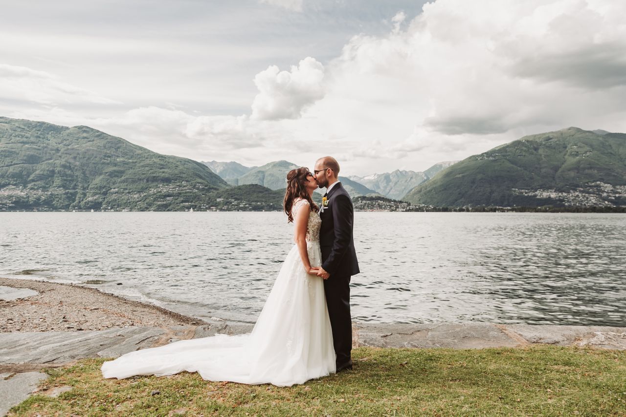 Bride and groom share a kiss by a scenic lake with mountains in the background.